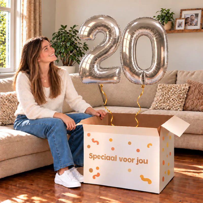 20 Jaar Cijfer Ballonnen Zilver met twee heliumgevulde cijferballonnen en een jarige in een warme woonkamer