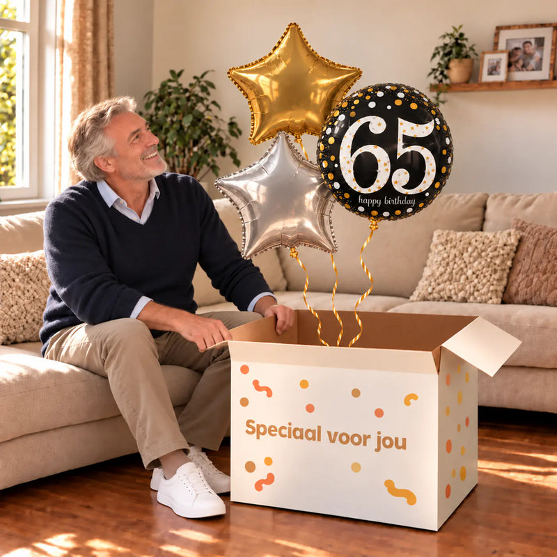 Een jarige met 65 Jaar Trosje Zilver/Zwart/Goud boven een open Speciaal voor jou-doos in een warme woonkamer.