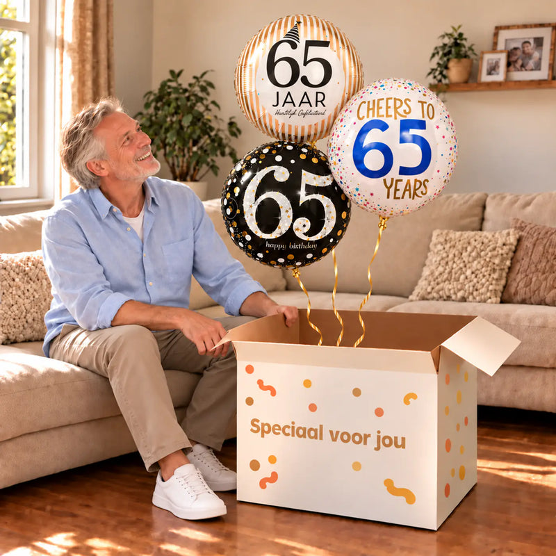 Een jarige met 65 Jaar Trosje Zwart/Goud/Zilver/Blauw boven een open Speciaal voor jou-doos in een warme woonkamer.