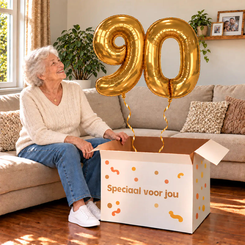 90 Jaar Cijfer Ballonnen Goud met twee heliumgevulde cijferballonnen en een jarige in een warme woonkamer