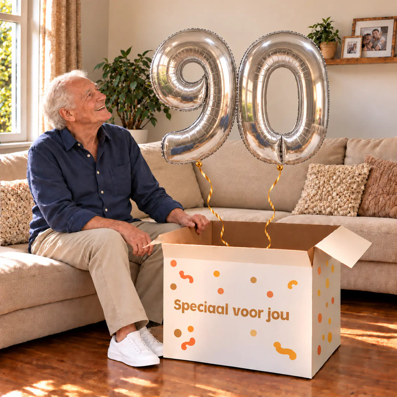 90 Jaar Cijfer Ballonnen Zilver met twee heliumgevulde cijferballonnen en een jarige in een warme woonkamer