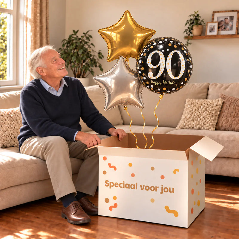 Een jarige met 90 Jaar Trosje Zilver/Zwart/Goud boven een open Speciaal voor jou-doos in een warme woonkamer.