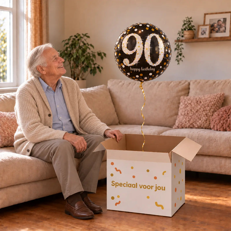 Man viert 90 jaar met 90 Jaar Ballon Zwart/Zilver/Goud uit een cadeaudoos van Ballonnenshop.nl