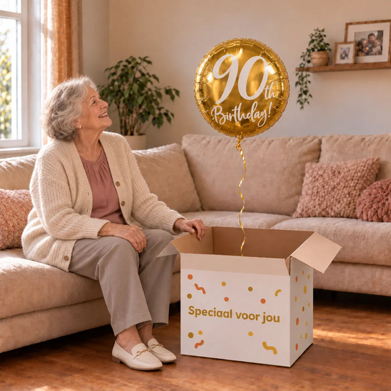 Vrouw viert 90 jaar met 90th Birthday Helium Ballon Goud uit een cadeaudoos van Ballonnenshop.nl