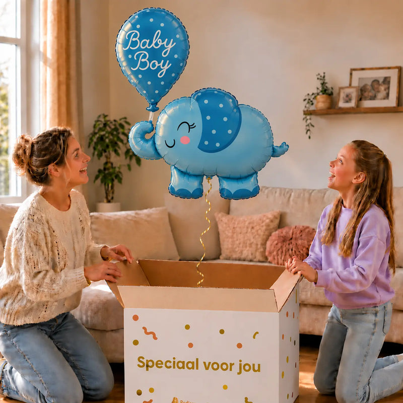 Baby Boy Blauw Olifantje XL zweeft boven een geopende cadeaudoos bij een moeder en meisje in een warme woonkamer.
