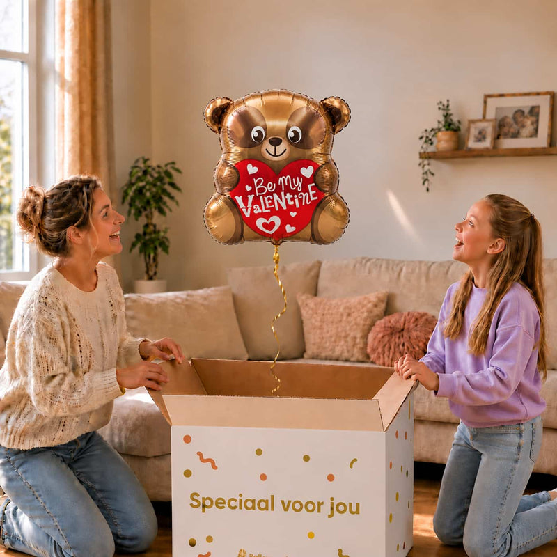 Moeder en meisje bekijken een Be My Valentine-beertjesballon van 45 cm met een rood hart boven een geopende cadeaudoos.