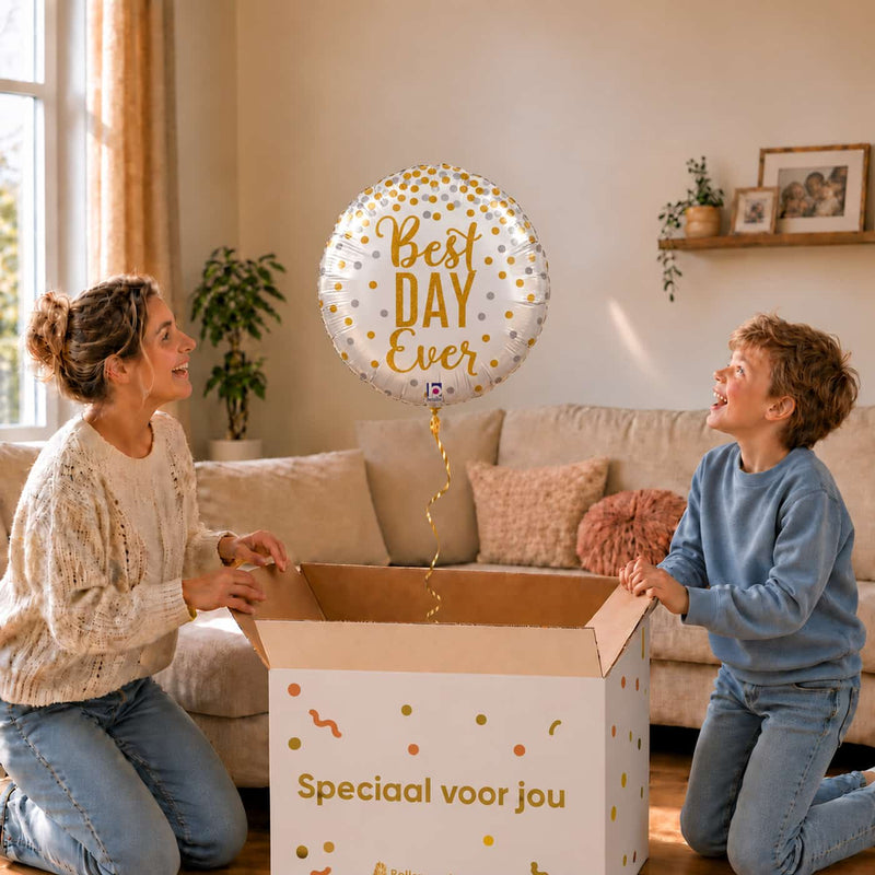 Moeder en jongen bekijken een Best Day Ever-ballon van 45 cm met gouden letters en confetti boven een geopende cadeaudoos.