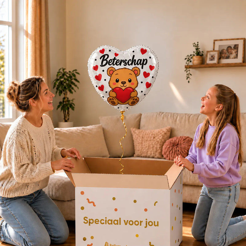 Moeder en meisje bekijken een hartvormige Beterschap-ballon van 46 cm met een beertje en rode hartjes boven een geopende cadeaudoos.