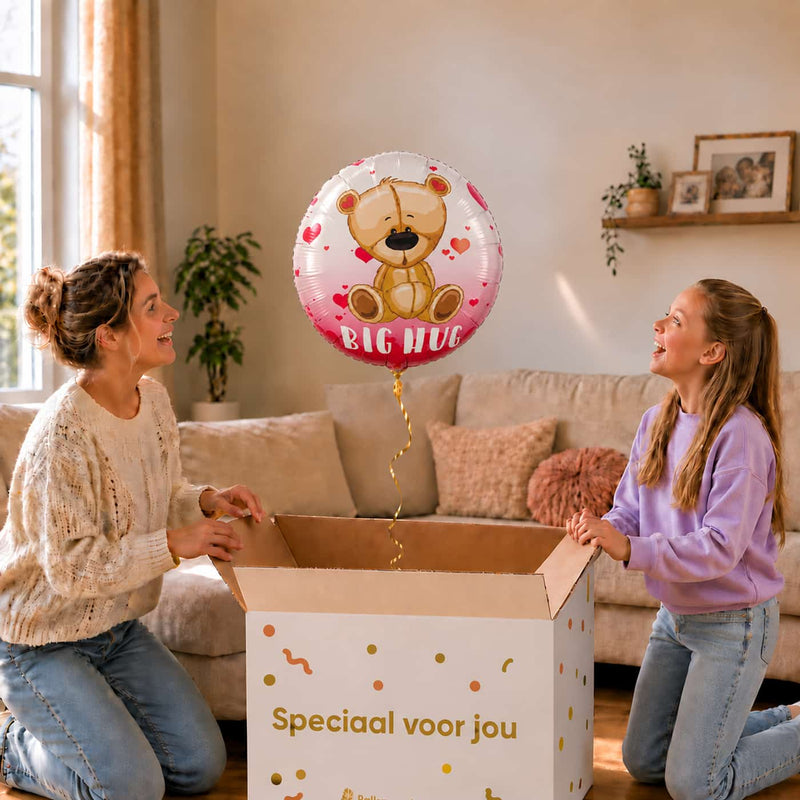 Moeder en meisje bekijken een Big Hug-ballon van 45 cm met een beertje en rode hartjes boven een geopende cadeaudoos.