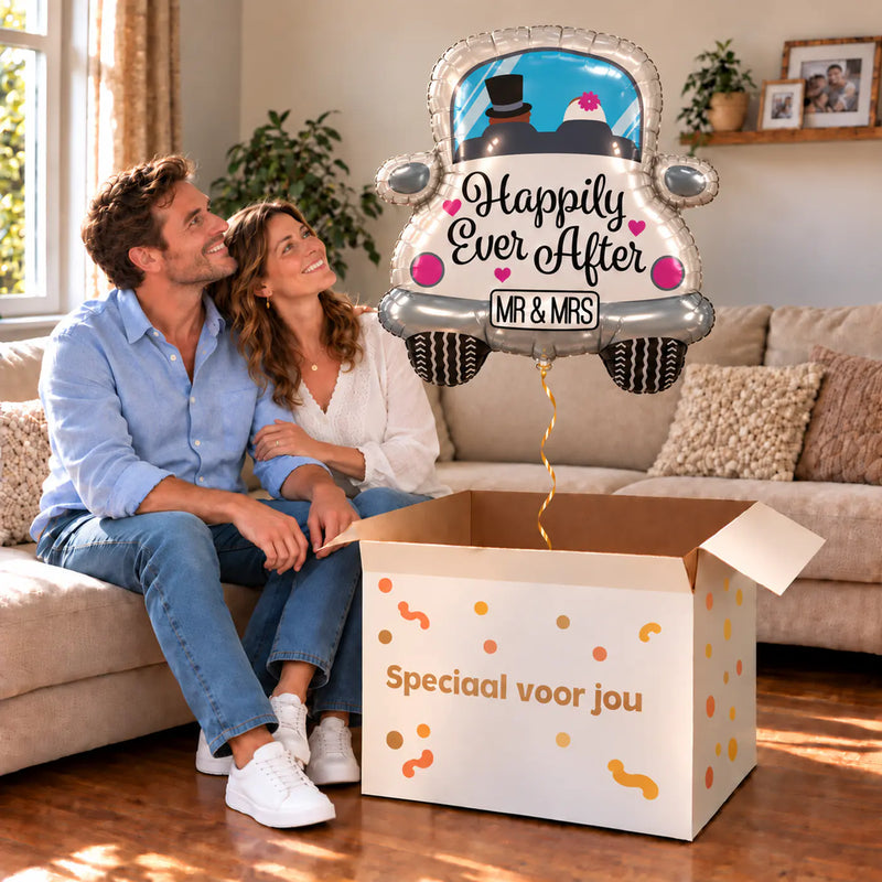 Een volwassen stel kijkt blij naar Happy Ever After Auto XL Ballon boven een grote Speciaal voor jou-doos in een warme woonkamer.