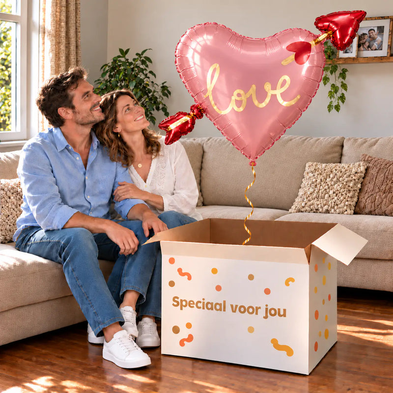 Een volwassen stel kijkt blij naar Hart Met Pijl Helium XL Ballon boven een grote Speciaal voor jou-doos in een warme woonkamer.