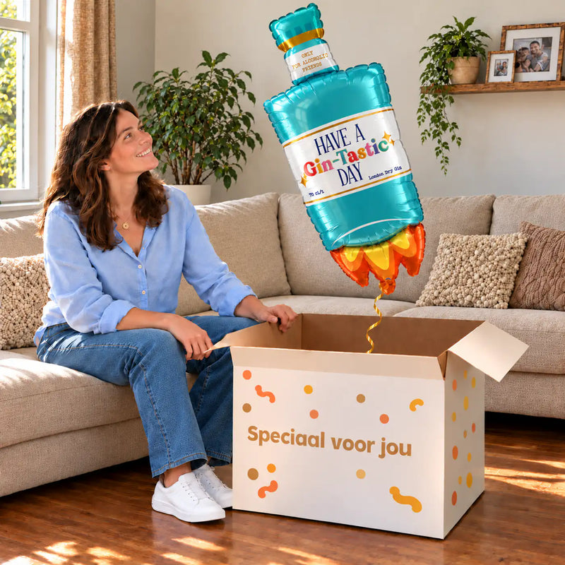Een vrouw kijkt blij naar Have A Gin – Tastic Day XL Ballon boven een grote Speciaal voor jou-doos in een warme woonkamer.