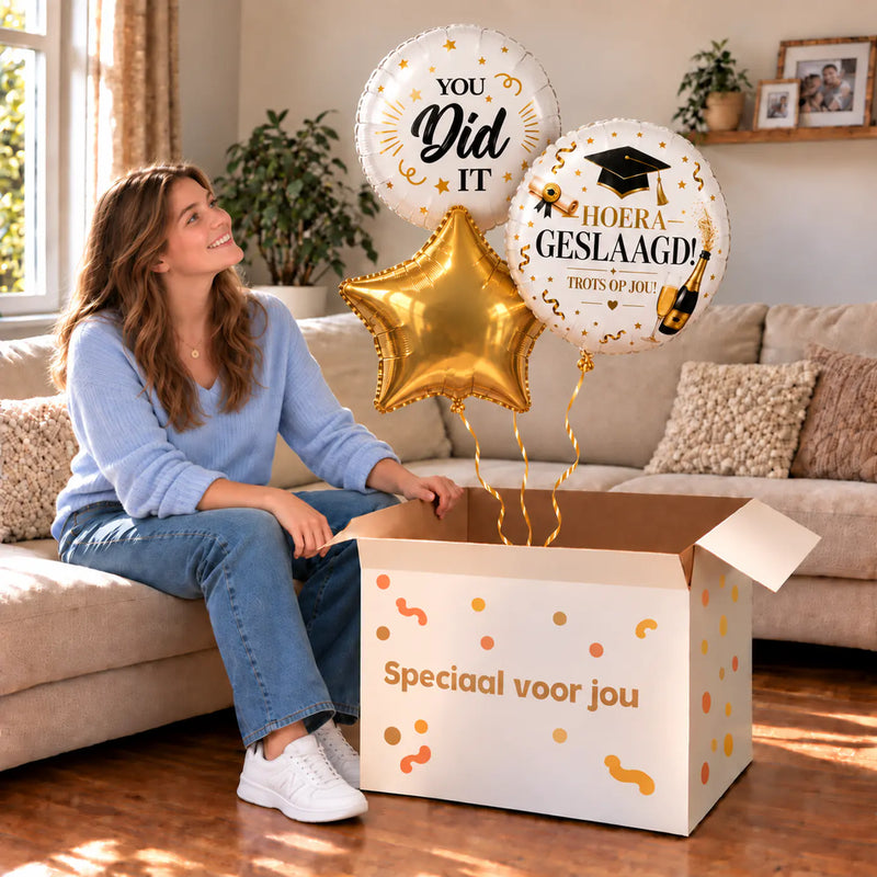 Een blije geslaagde met Hoera Geslaagd Ballonnentros - Gevuld Met Helium - 45 cm boven een open Speciaal voor jou-doos in een warme woonkamer.