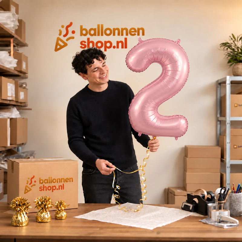 Jesse houdt de 2 Jaar Cijfer Pastel Roze XL vast in de warme inpakruimte van Ballonnenshop.nl.