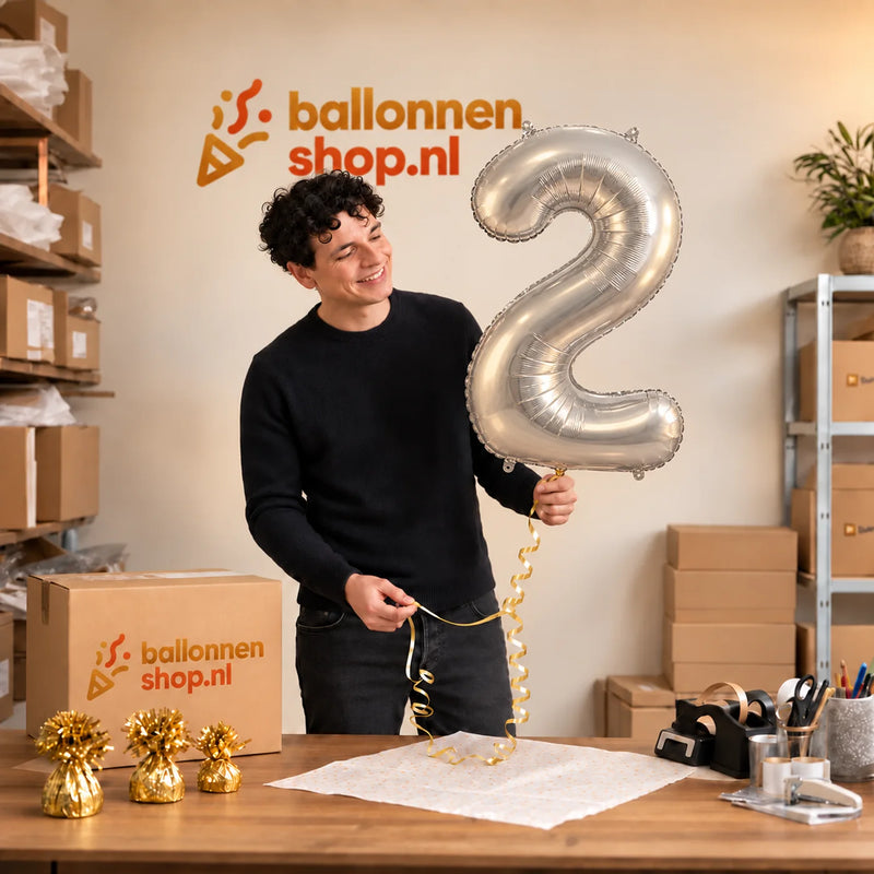 Jesse houdt de 2 Jaar Cijfer Zilver XL Ballon vast in de warme inpakruimte van Ballonnenshop.nl.