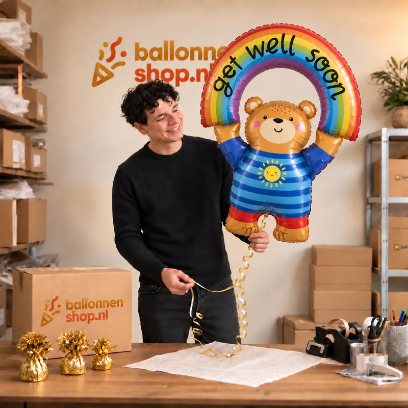 Jesse houdt de Beer Get Well Soon Regenboog XL vast in de warme inpakruimte van Ballonnenshop.nl.