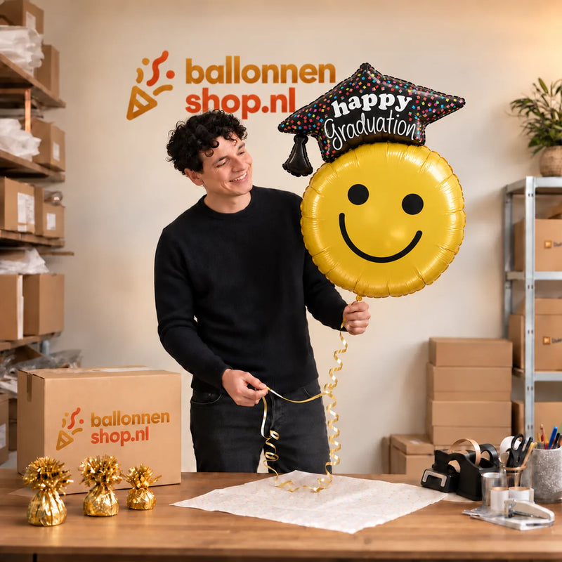 Jesse houdt de Graduation Smiley XL Ballon vast in de warme inpakruimte van Ballonnenshop.nl.