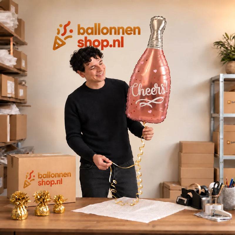 Jesse houdt de Wijnfles Cheers Helium Ballon vast in de warme inpakruimte van Ballonnenshop.nl.