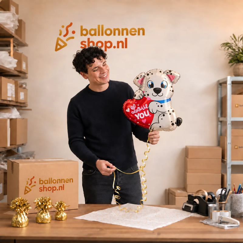 Jesse houdt de Love You Hondje Ballon vast in de warme werkplaats van Ballonnenshop.nl.