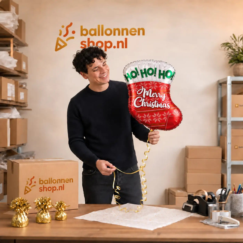 Jesse houdt de Merry Christmas Sok Helium Ballon vast in de warme werkplaats van Ballonnenshop.nl.