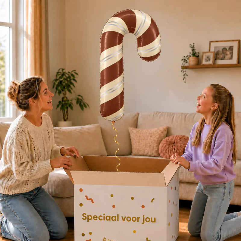 Satijnchocolade Kerst Zuurstok XL – uitpakmoment met moeder en meisje in een warme woonkamer – Ballonnenshop.nl