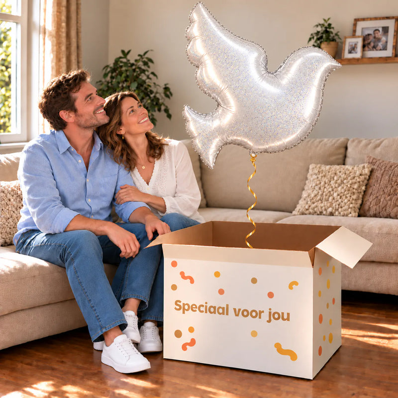 Een volwassen stel kijkt blij naar Witte Duif Helium XL Ballon boven een grote Speciaal voor jou-doos in een warme woonkamer.