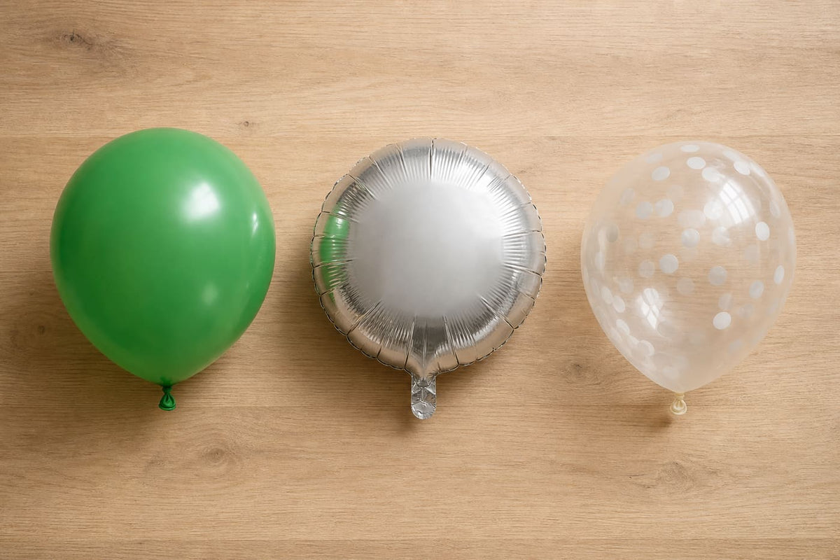 Een groene latexballon, zilveren folieballon en transparante confettiballon liggen naast elkaar.