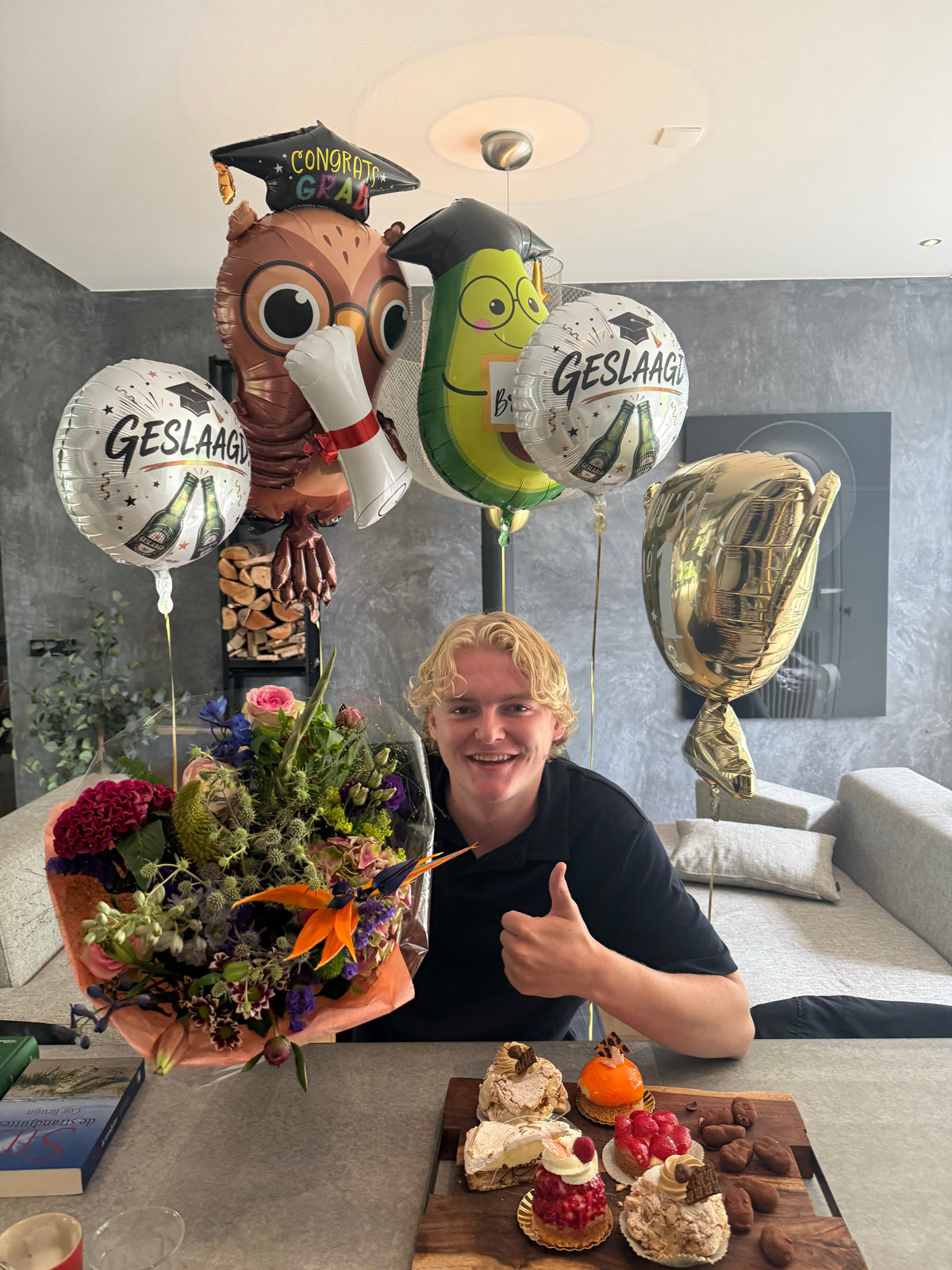 Sil viert dat hij geslaagd is voor zijn examens, met ballonnen, bloemen en gebak.