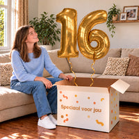 16 Jaar Cijfer Ballonnen Goud met twee heliumgevulde cijferballonnen en een jarige in een warme woonkamer