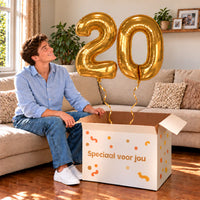 20 Jaar Cijfer Ballonnen Goud met twee heliumgevulde cijferballonnen en een jarige in een warme woonkamer