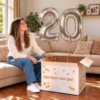 20 Jaar Cijfer Ballonnen Zilver met twee heliumgevulde cijferballonnen en een jarige in een warme woonkamer
