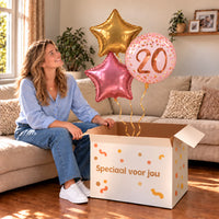 Een jarige met 20 Jaar Trosje Roze/Goud/Rose Goud boven een open Speciaal voor jou-doos in een warme woonkamer.
