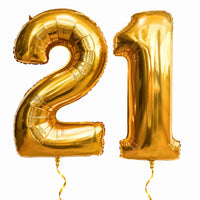 21 Jaar Cijfer Ballonnen Goud – heliumgevulde ballonnen met dunne gouden lintjes op een witte achtergrond