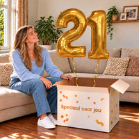 21 Jaar Cijfer Ballonnen Goud met twee heliumgevulde cijferballonnen en een jarige in een warme woonkamer