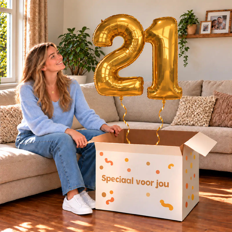 21 Jaar Cijfer Ballonnen Goud met twee heliumgevulde cijferballonnen en een jarige in een warme woonkamer