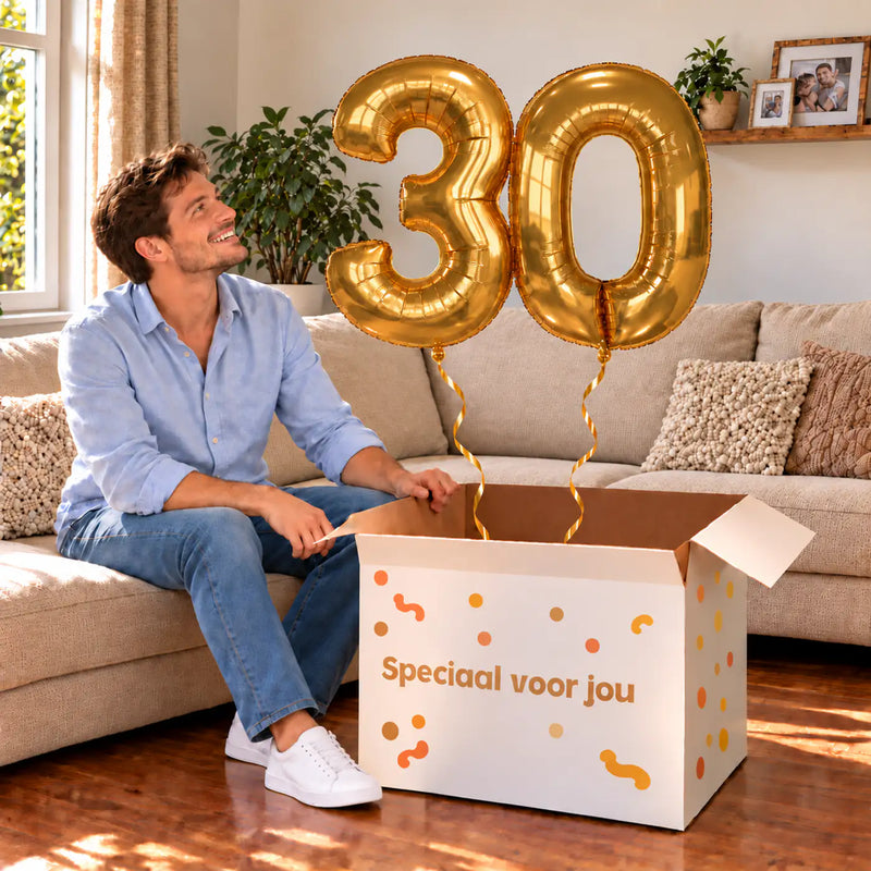 30 Jaar Cijfer Ballonnen Goud met twee heliumgevulde cijferballonnen en een jarige in een warme woonkamer