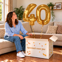 40 Jaar Cijfer Ballonnen Goud met twee heliumgevulde cijferballonnen en een jarige in een warme woonkamer