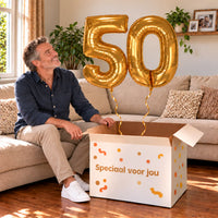 50 Jaar Cijfer Ballonnen Goud met twee heliumgevulde cijferballonnen en een jarige in een warme woonkamer