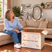50 Jaar Cijfer Ballonnen Zilver met twee heliumgevulde cijferballonnen en een jarige in een warme woonkamer