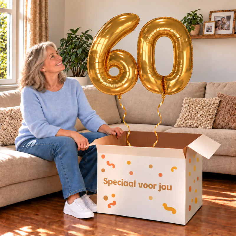 60 Jaar Cijfer Ballonnen Goud met twee heliumgevulde cijferballonnen en een jarige in een warme woonkamer