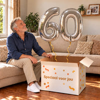60 Jaar Cijfer Ballonnen Zilver met twee heliumgevulde cijferballonnen en een jarige in een warme woonkamer