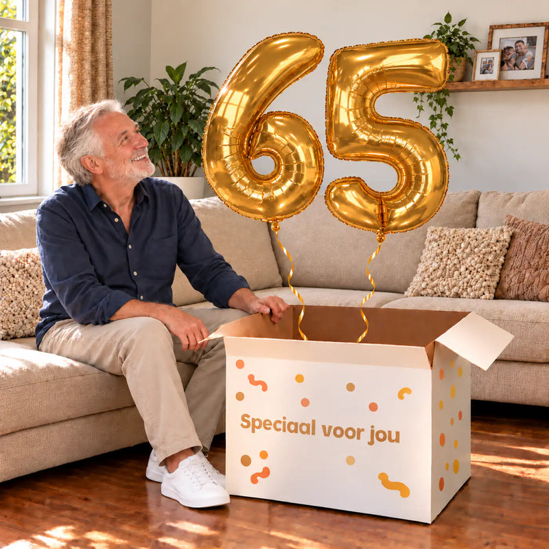 65 Jaar Cijfer Ballonnen Goud met twee heliumgevulde cijferballonnen en een jarige in een warme woonkamer