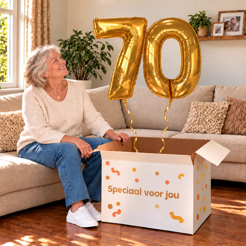 70 Jaar Cijfer Ballonnen Goud met twee heliumgevulde cijferballonnen en een jarige in een warme woonkamer