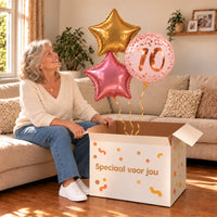 Een jarige met 70 Jaar Trosje Roze/Goud/Rose Goud boven een open Speciaal voor jou-doos in een warme woonkamer.