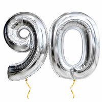 90 Jaar Cijfer Ballonnen Zilver – heliumgevulde ballonnen met dunne gouden lintjes op een witte achtergrond