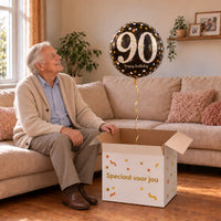 Man viert 90 jaar met 90 Jaar Ballon Zwart/Zilver/Goud uit een cadeaudoos van Ballonnenshop.nl
