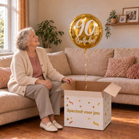 Vrouw viert 90 jaar met 90th Birthday Helium Ballon Goud uit een cadeaudoos van Ballonnenshop.nl