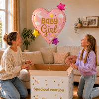 Baby Girl Hart Sterren XL Ballon zweeft boven een geopende cadeaudoos bij een moeder en meisje in een warme woonkamer.