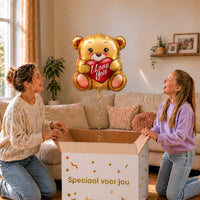 Moeder en meisje bekijken een gouden I Love You-beertjesballon van 45 cm met een rood hart boven een geopende cadeaudoos.