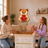 Moeder en meisje bekijken een beertjesballon van 45 cm met een rood I Love You-hart boven een geopende cadeaudoos.